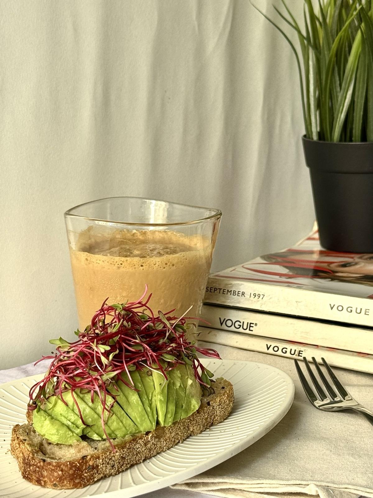 Avocado toast topped with fresh microgreens beside a coffee